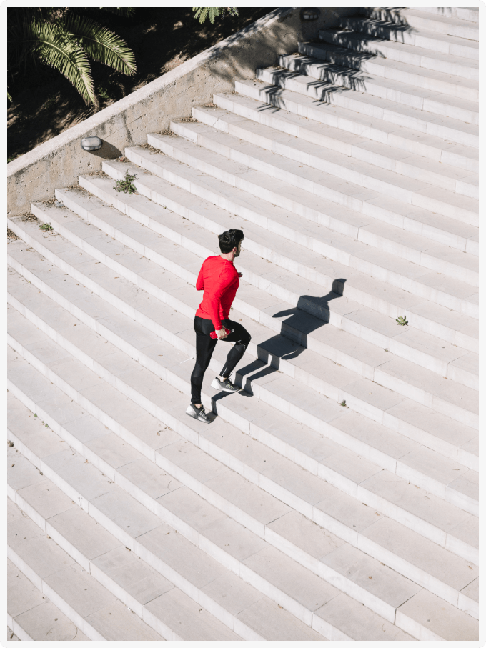 Sportoló férfi piros felsőben lépcsőn fut felfelé, szimbolikus küzdelem és fejlődés képe.